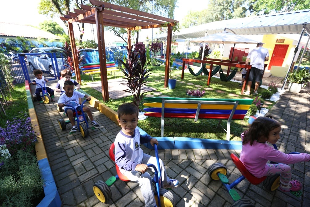 Crianças brincando em área externa de escola infantil, com brinquedos coloridos