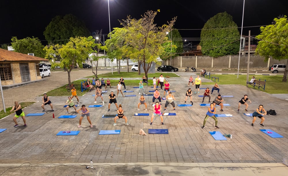 Aula coletiva de ginástica ao ar livre, com colchonetes e participantes em parque urbano