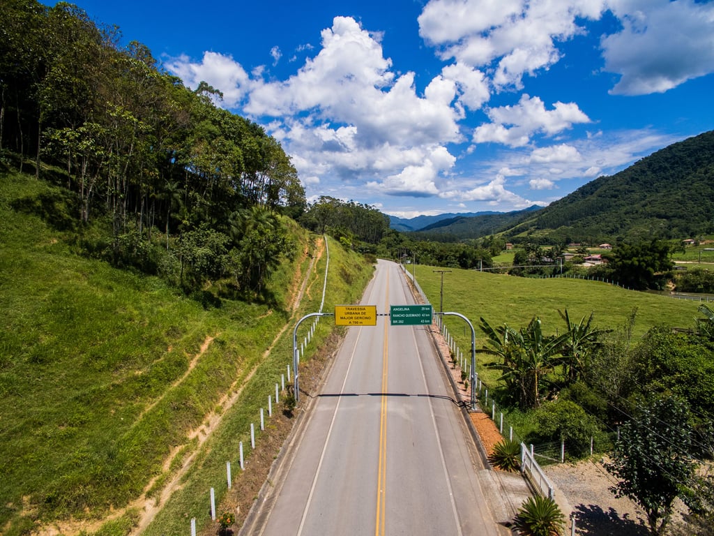 Estrada no interior de Major Gercino SC, cercada por morros e vegetação, em dia claro