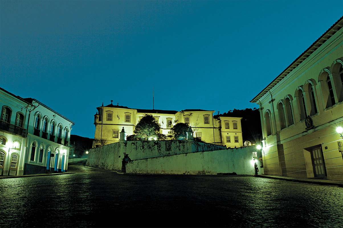 Fachada da Escola de Minas da UFOP, com arquitetura histórica iluminada à noite.