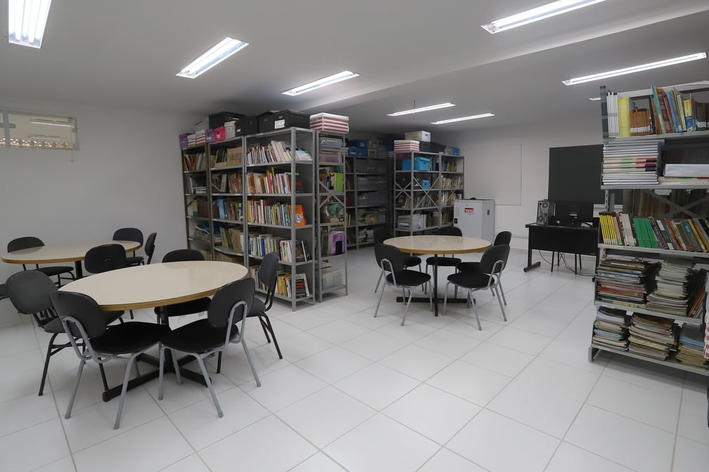 Sala de aula organizada em escola pública, com mesas e prateleiras de livros