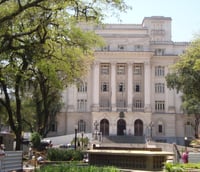 Praça central arborizada em José Bonifácio SP, em dia ensolarado, com edifício público ao fundo