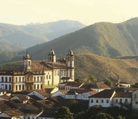 Paisagem urbana de pequena cidade no interior de Minas Gerais, com igreja e montanhas ao fundo ao entardecer