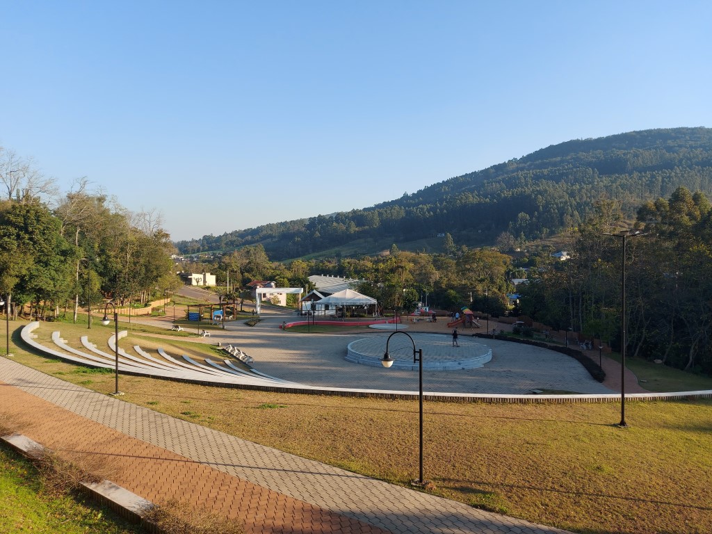 Vista aérea de praça central em Tupandi RS, com áreas verdes e morros ao fundo