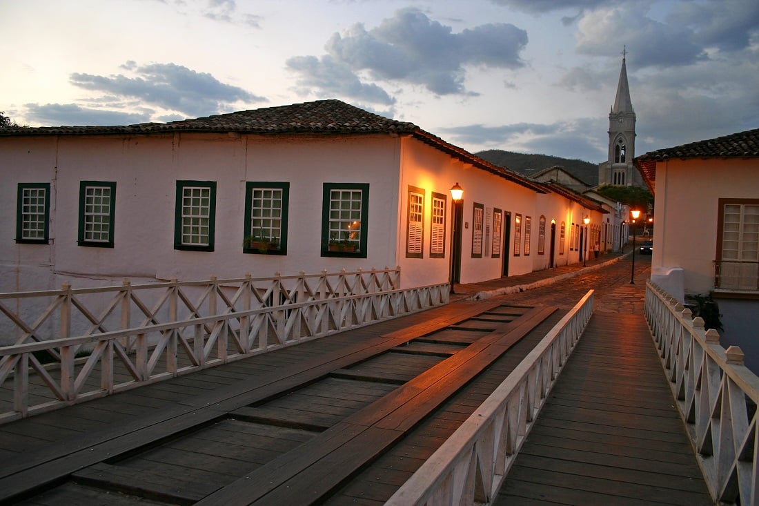 Centro histórico da Cidade de Goiás ao entardecer, com casario colonial e ponte de madeira sobre o Rio Vermelho