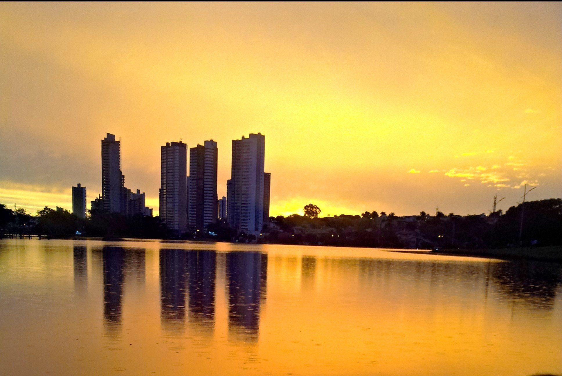 Vista aérea de Campo Grande MS ao entardecer, com prédios refletidos na água.