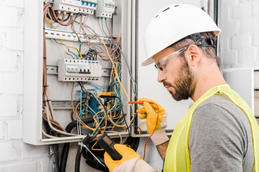 Técnico de manutenção elétrica inspecionando painel elétrico em ambiente hospitalar, utilizando EPI completo