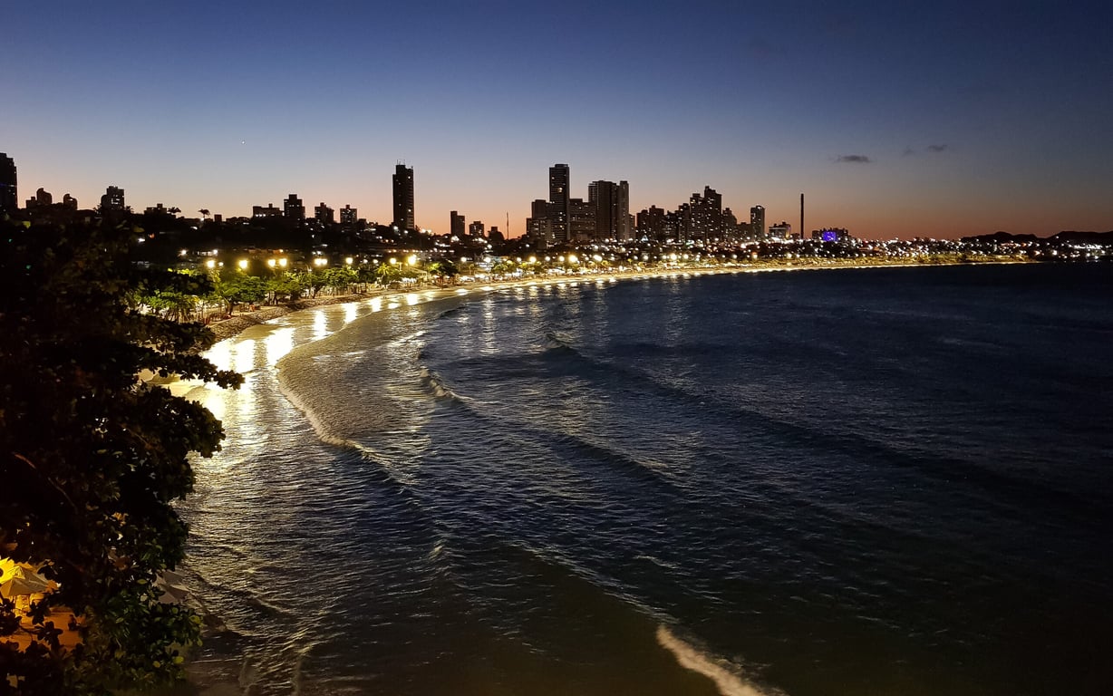 Vista aérea de Natal RN, com a praia de Ponta Negra e o Morro do Careca ao fundo, ao pôr do sol.