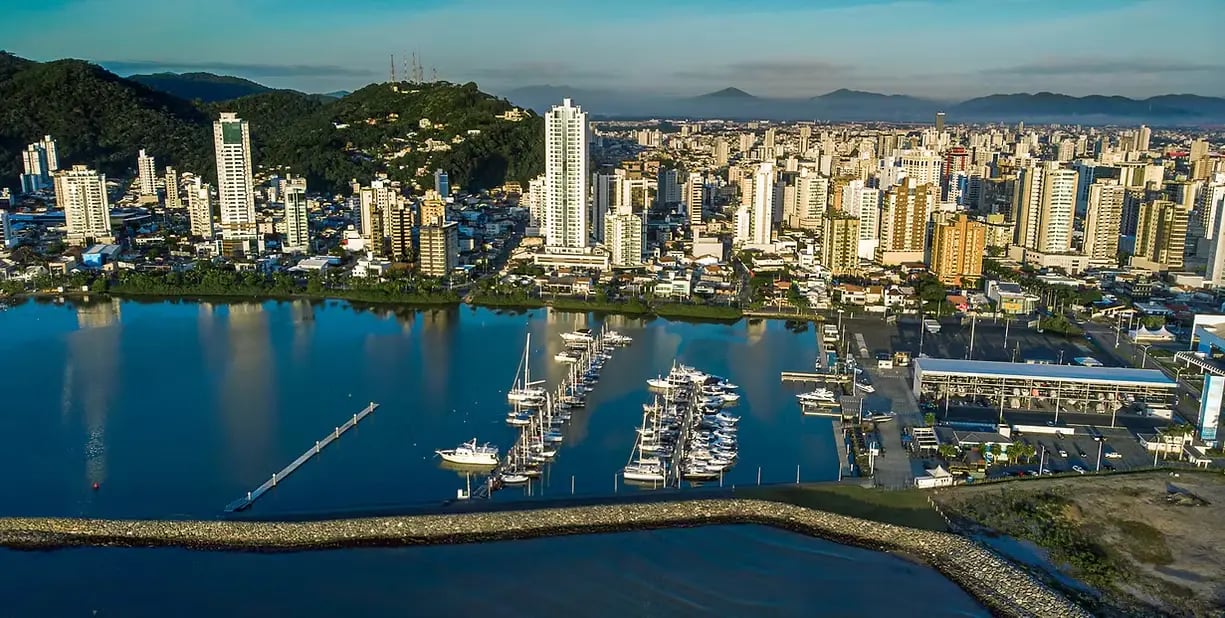 Centro de Itajaí às margens do Rio Itajaí-Açu, com ponte e embarcações ao entardecer.