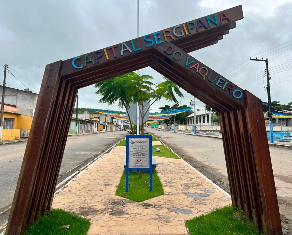 Arco de entrada de Pedra Mole SE em dia nublado, com rua arborizada ao fundo.