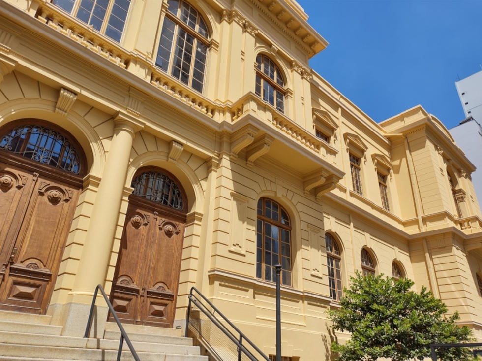 Fachada do campus da Unicamp com estudantes caminhando em dia claro