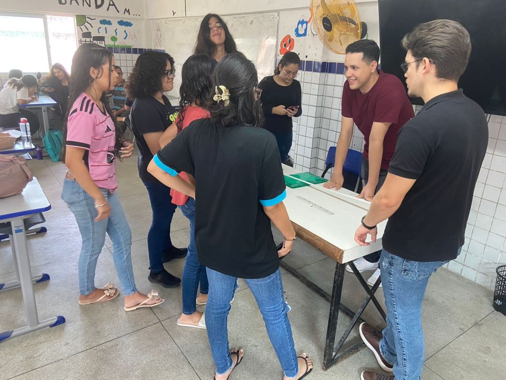 Sala de aula universitária, com professor explicando conteúdo no quadro e estudantes atentos