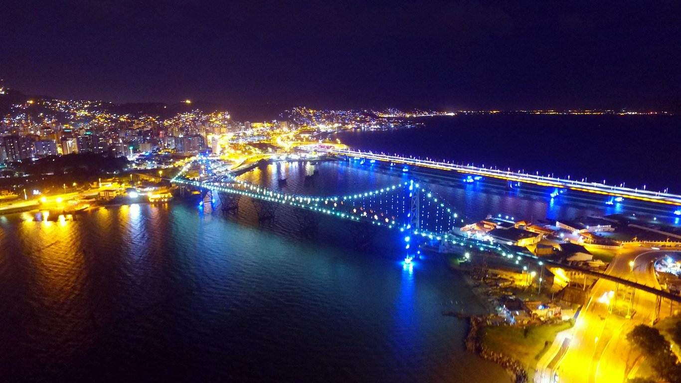 Vista aérea de Florianópolis com a Ponte Hercílio Luz iluminada ao entardecer