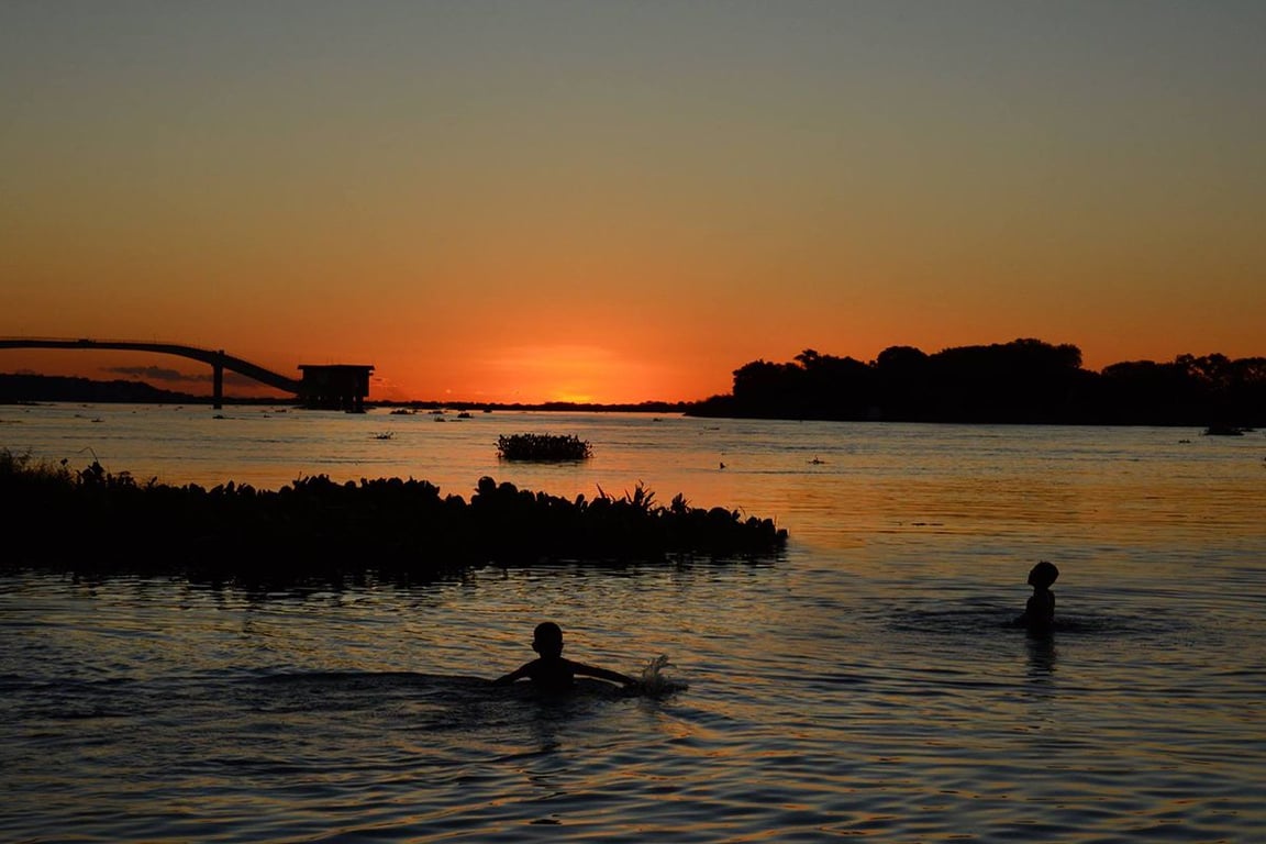 Rio Paraguai ao pôr do sol, com banhistas e vegetação ribeirinha