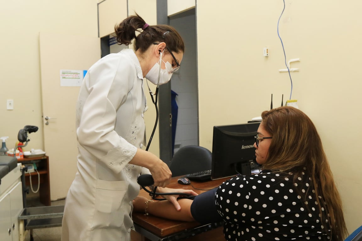 Profissional de saúde medindo a pressão arterial de paciente em consultório, com jaleco e estetoscópio