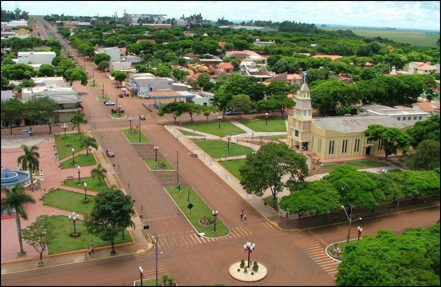 Vista aérea de cidade do interior do Paraná, com praça central e igreja ao fundo, no fim da tarde