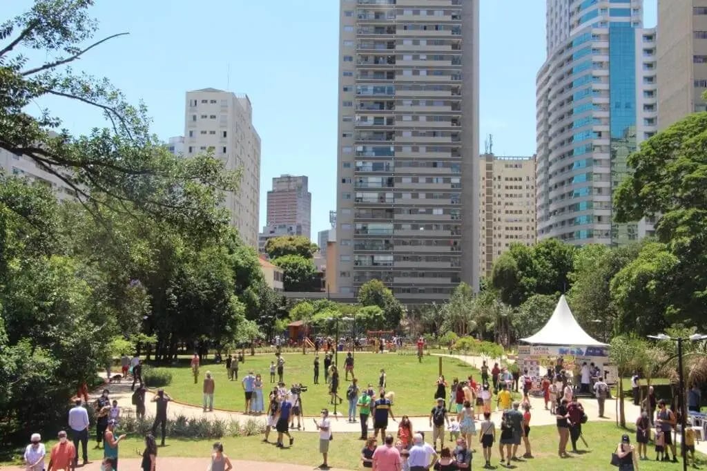 Parque urbano no interior paulista, fim de tarde, com pessoas caminhando e prédios baixos ao fundo