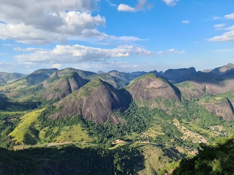 Paisagem rural no interior do Espírito Santo ao entardecer, com colinas verdes e lavouras, estrada vicinal e céu alaranjado