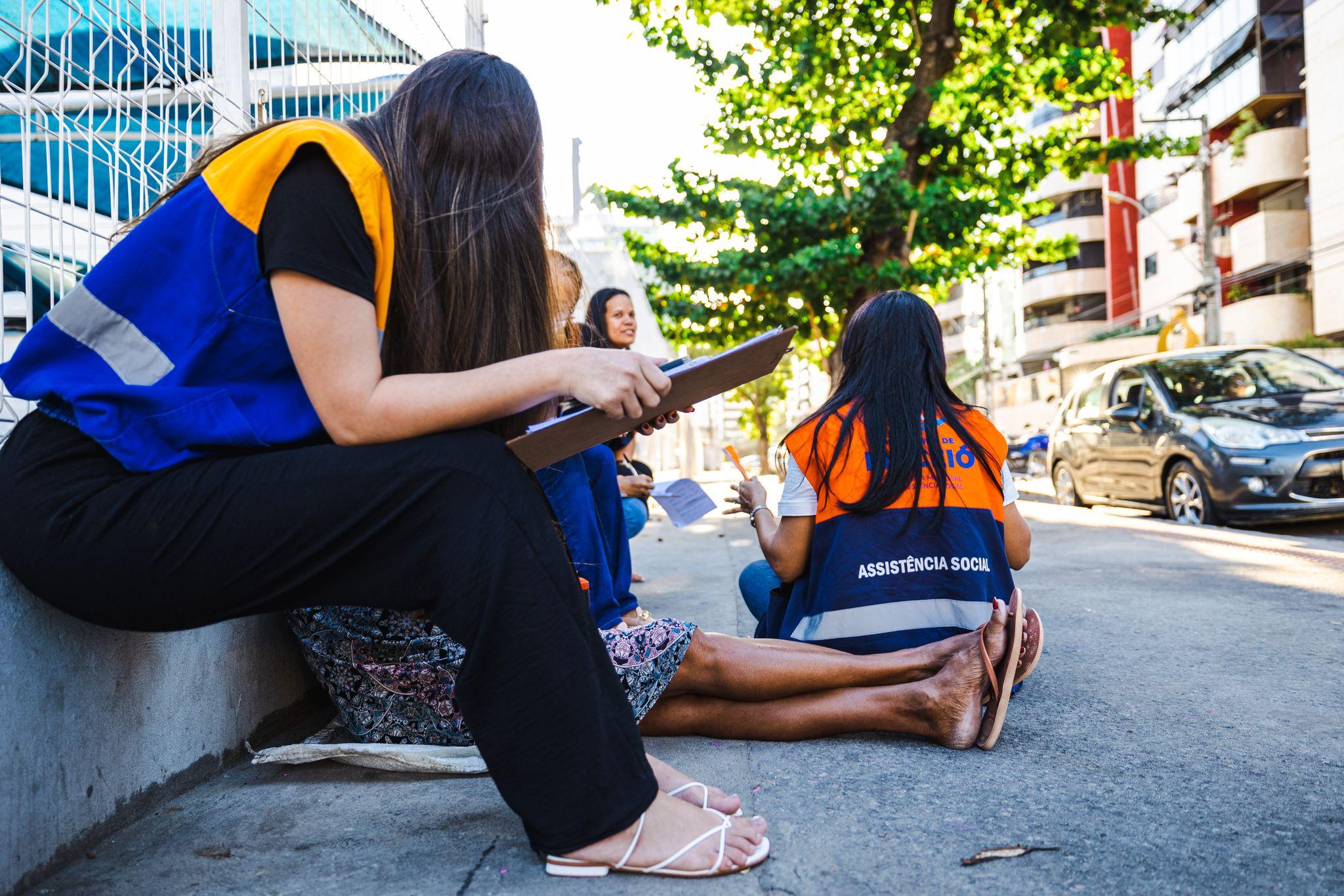 Equipe feminina de profissionais de serviço social em atividade de campo, com pranchetas, em ambiente urbano