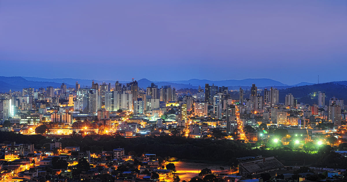 Panorama urbano de Divinópolis à noite, com a área central e o rio Itapecerica ao fundo