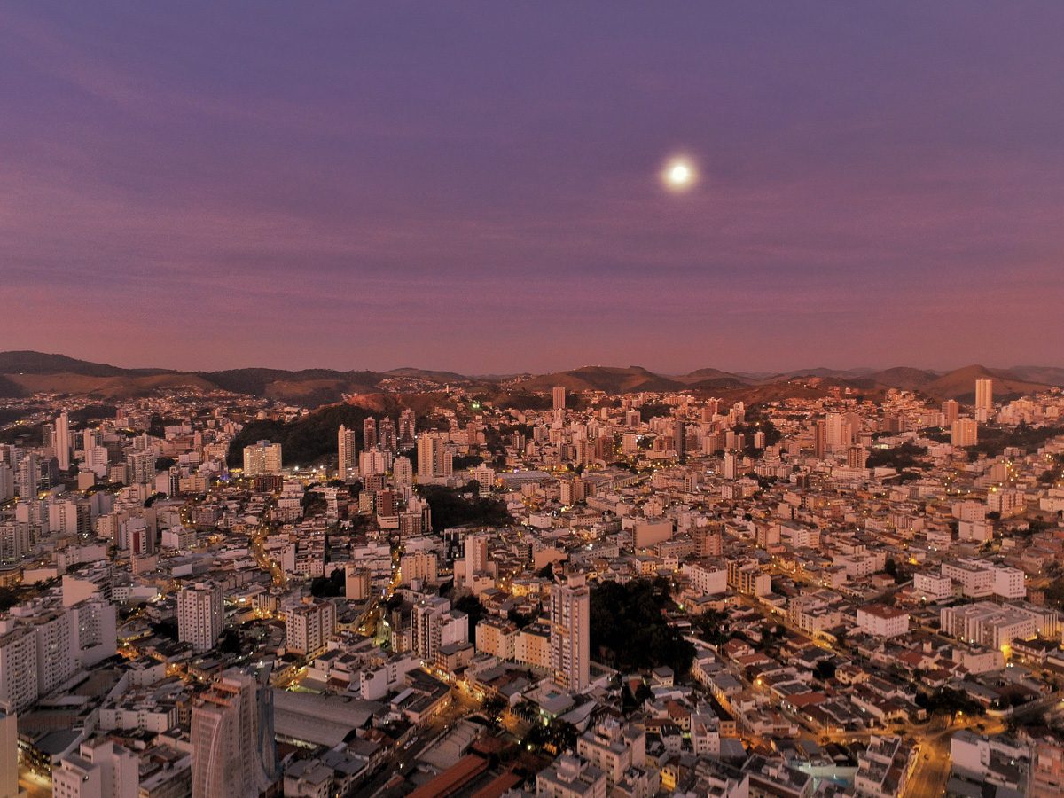 Panorama urbano de Juiz de Fora ao entardecer, com morros e prédios em destaque