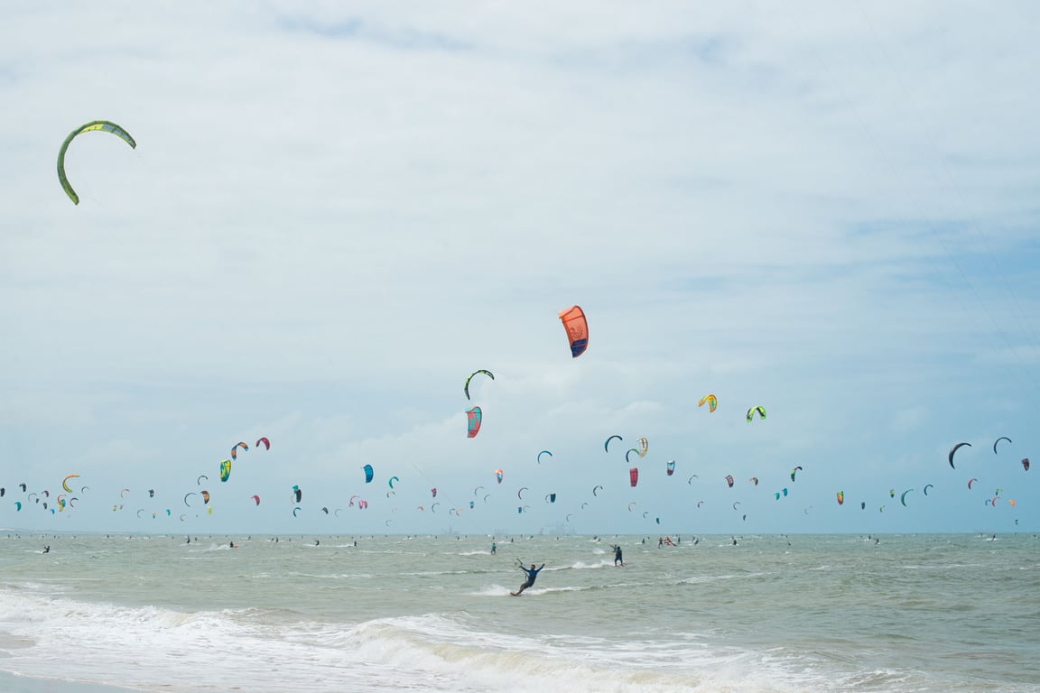 Litoral de Itapipoca ao pôr do sol, com kitesurfistas e dunas ao fundo