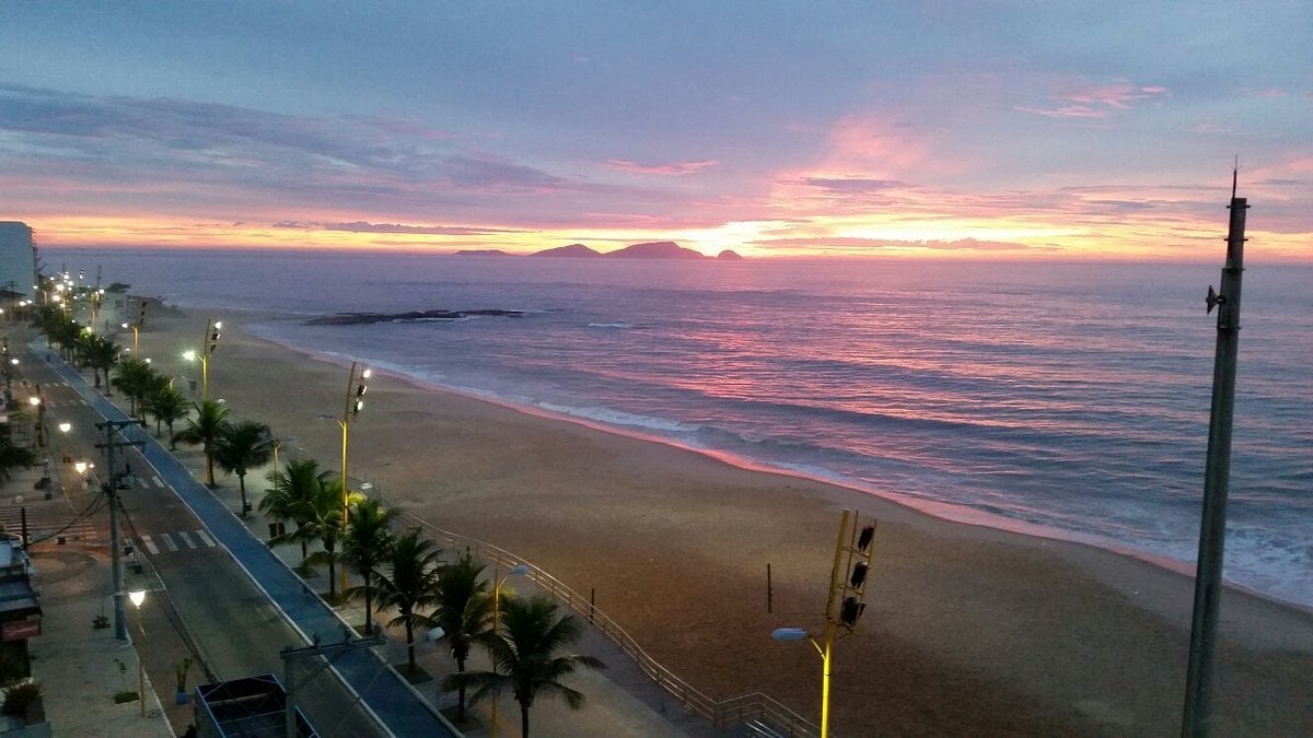 Orla de Macaé RJ ao amanhecer, com praia e mar sob céu colorido.