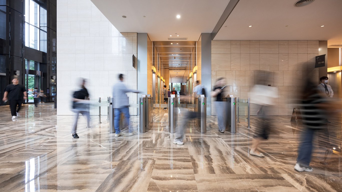 Entrada de prédio público moderno com catracas e fluxo moderado de pessoas, ilustrando controle de acesso