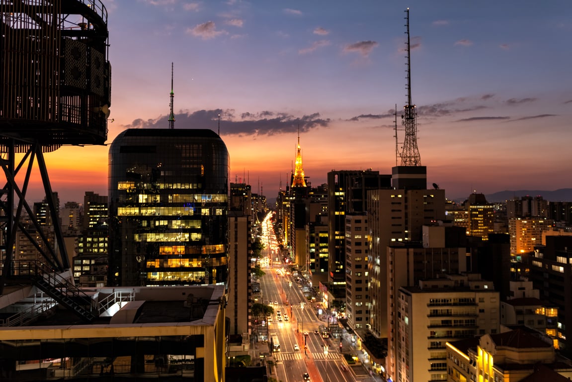 Skyline de São Paulo ao entardecer, com prédios na Avenida Paulista e movimento urbano