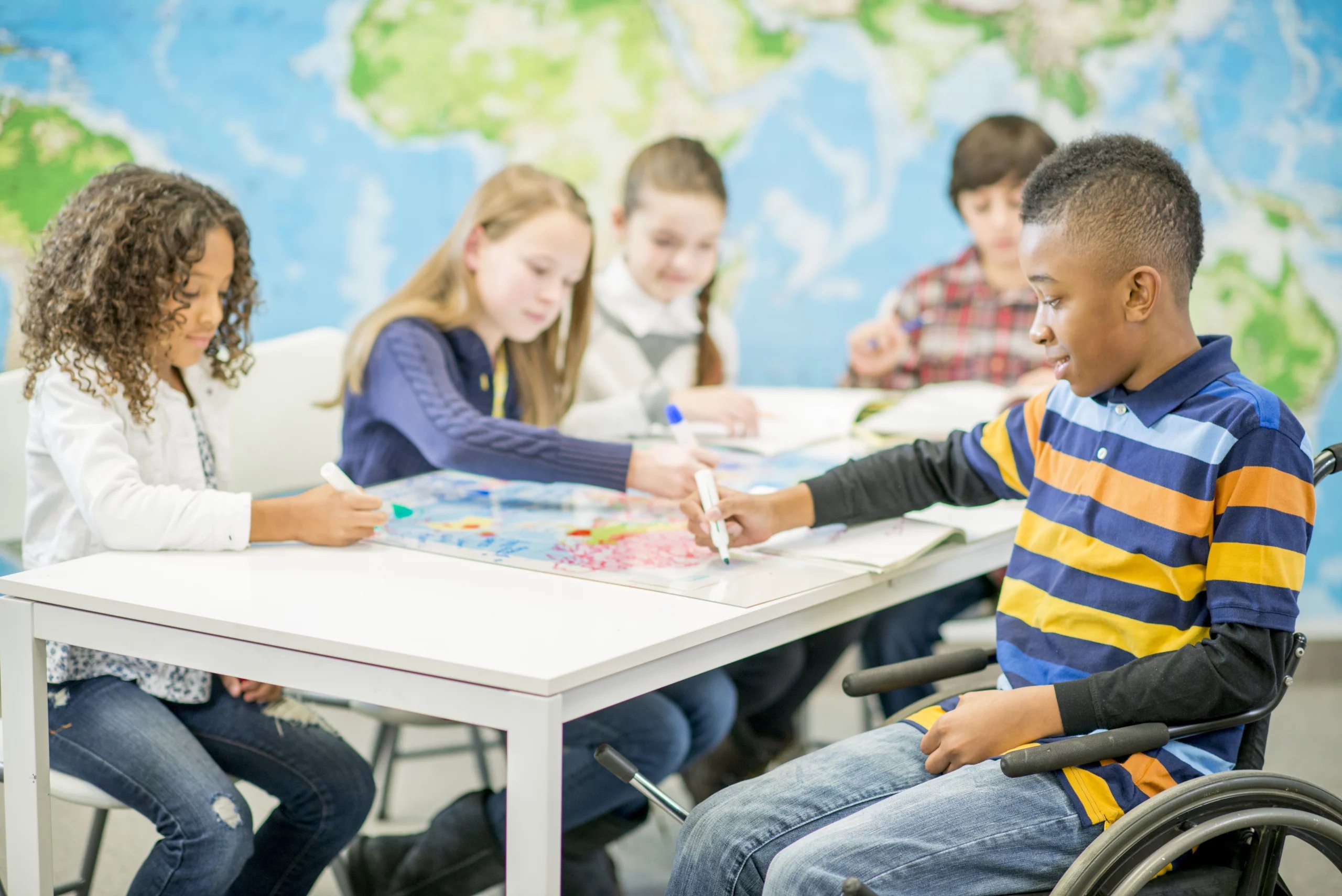 Sala de aula inclusiva com crianças e um estudante em cadeira de rodas participando de atividade educacional