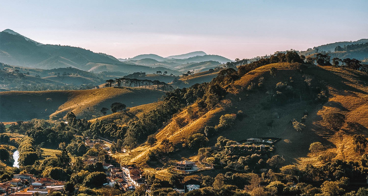 Vista do Sul de Minas ao entardecer, com montanhas e lago, em composição horizontal