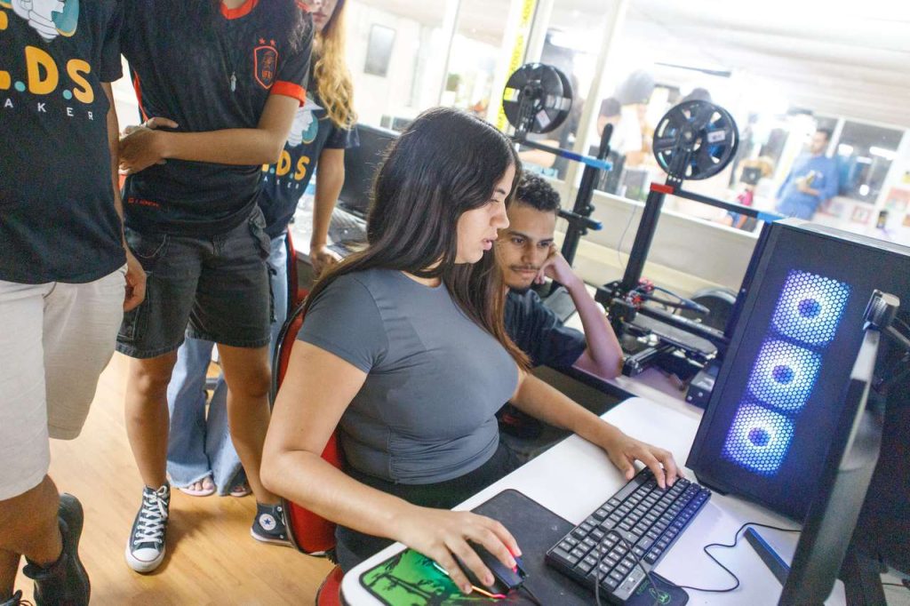 Equipe técnica em laboratório de informática universitário, com telas de código e servidores ao fundo