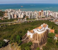 Vista aérea do Convento da Penha em Vila Velha, com a orla e o mar ao fundo, ao entardecer (Foto: Destinos Notáveis).