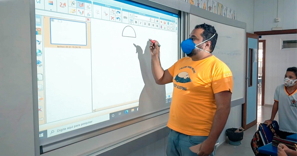 Professor em sala de aula moderna utilizando quadro interativo, estudantes atentos