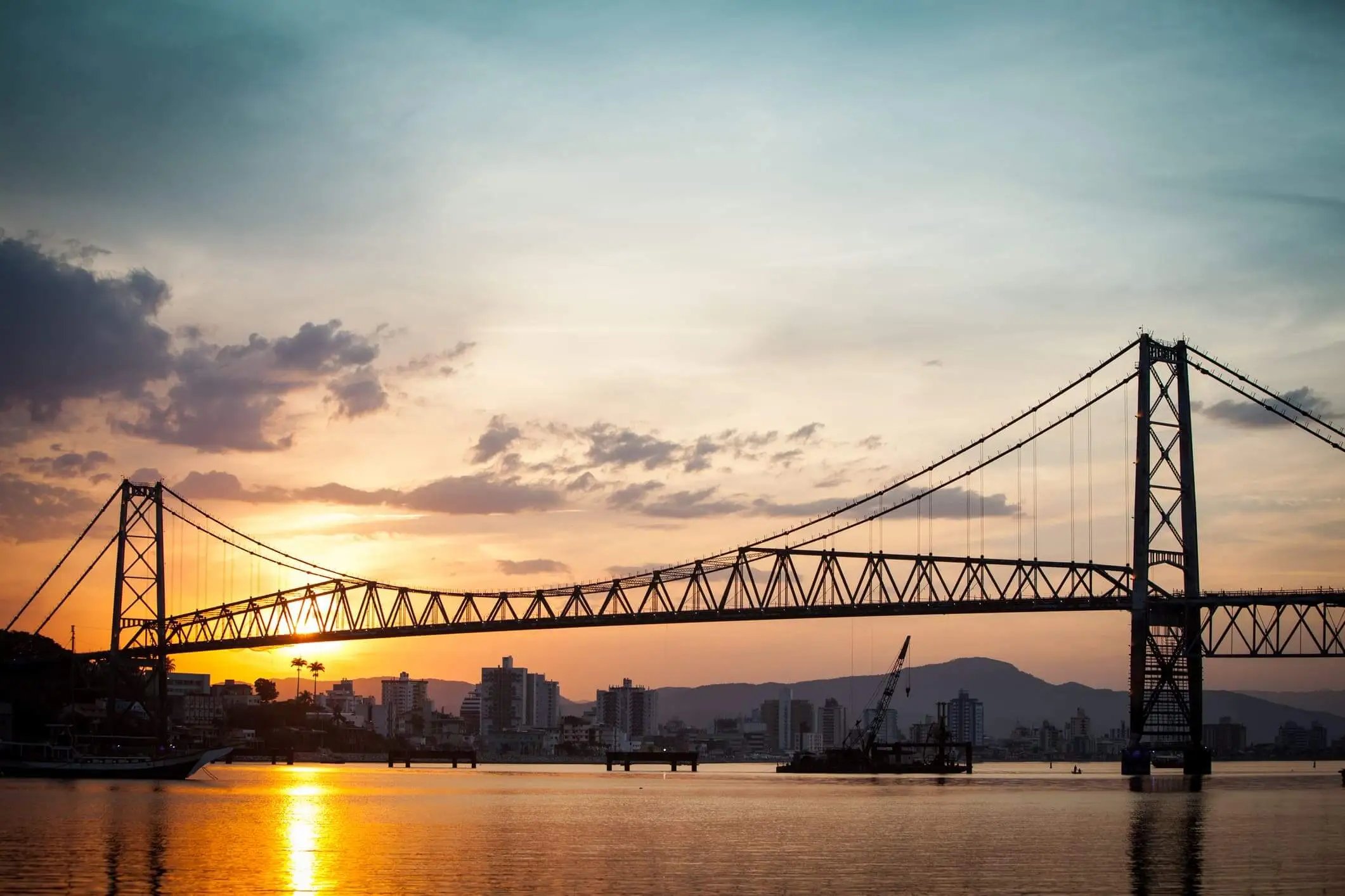 Vista panorâmica de Florianópolis ao entardecer, com a Ponte Hercílio Luz e a baía ao fundo
