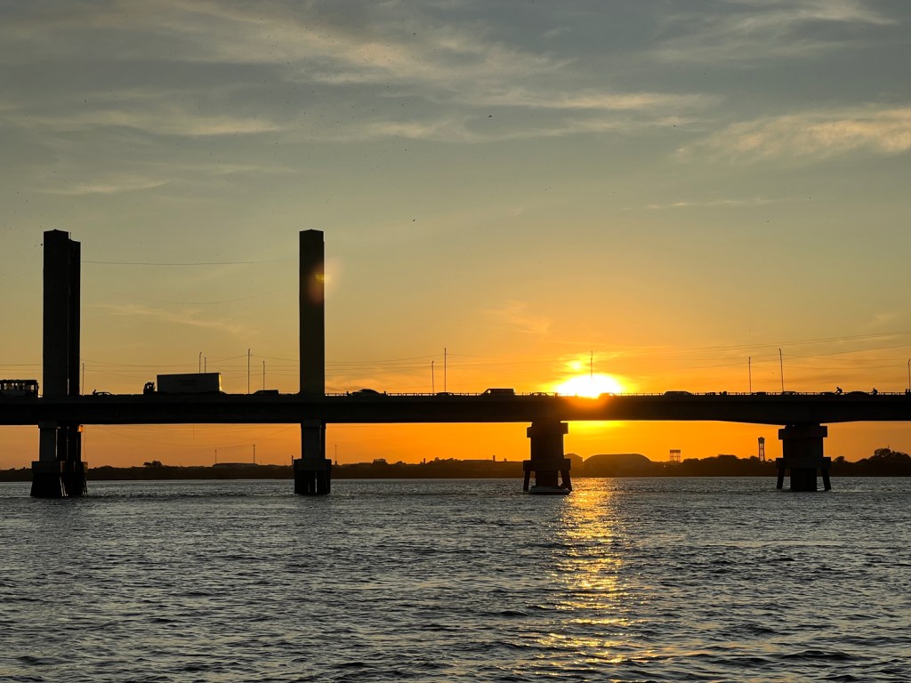 Orla do Rio São Francisco ao entardecer, com barcos e luzes urbanas ao fundo