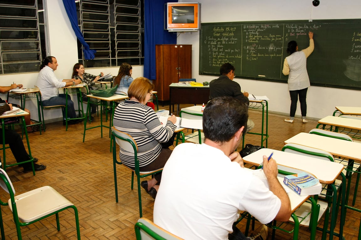 Sala de aula de EJA, com adultos e professora ao quadro