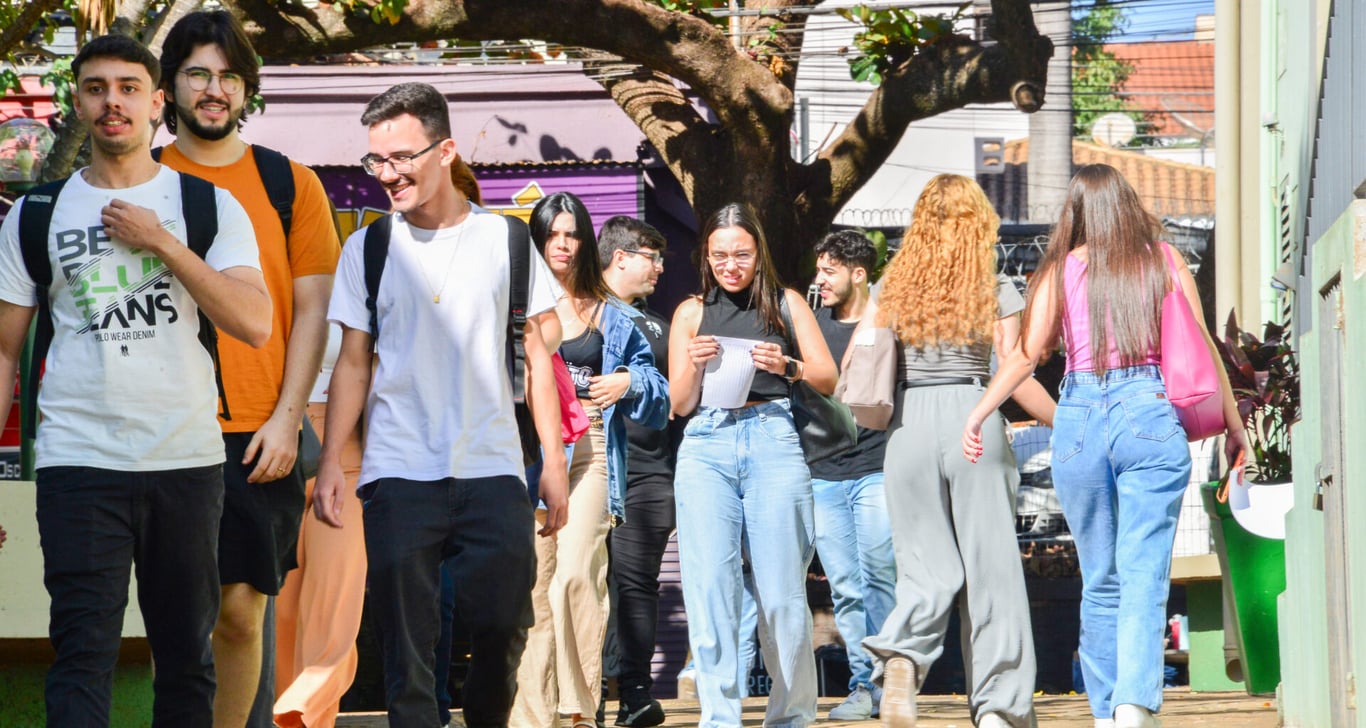Imagem de campus universitário público, com estudantes circulando entre prédios e áreas verdes