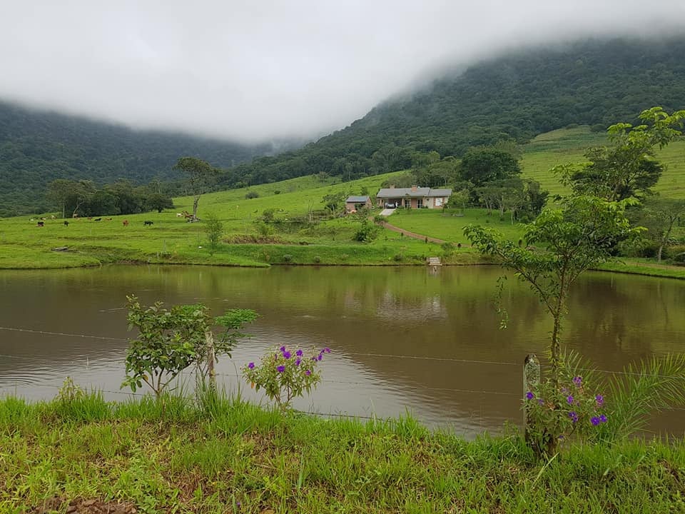Paisagem da região da Quarta Colônia, área rural com morros, lago e vegetação nativa, sob céu aberto