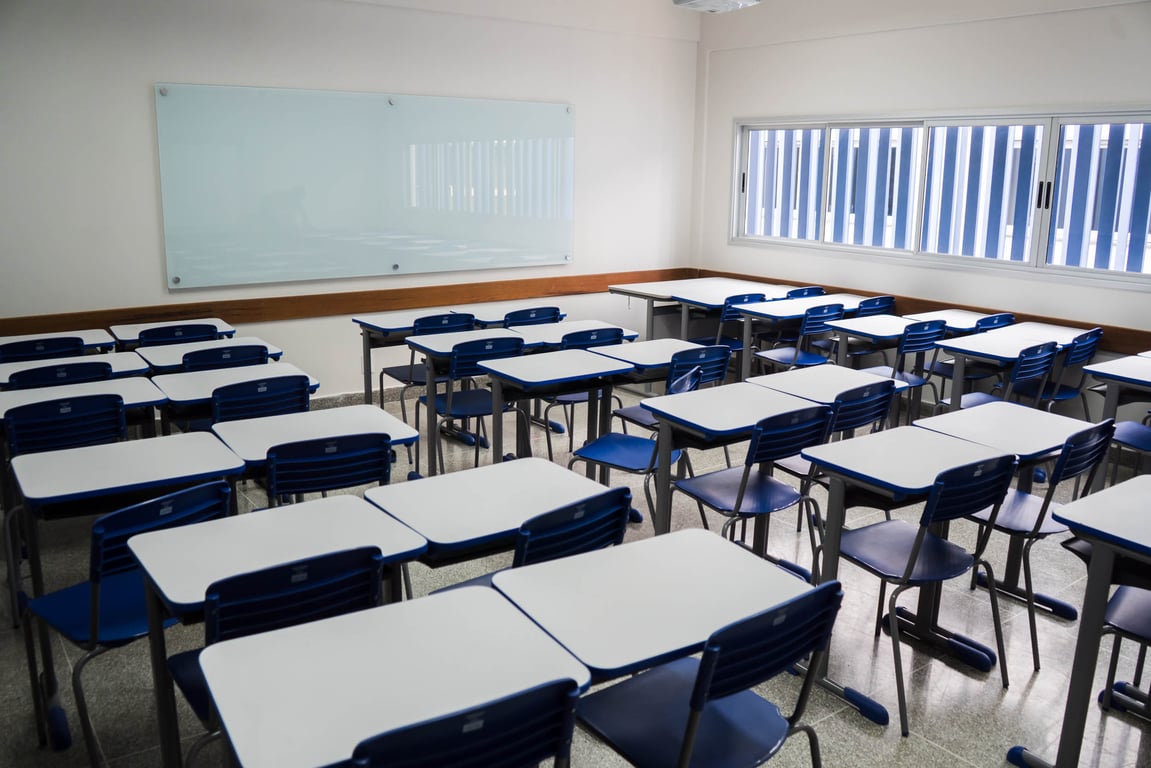Sala de aula de escola pública com carteiras e quadro, ambiente iluminado, representando a rotina docente