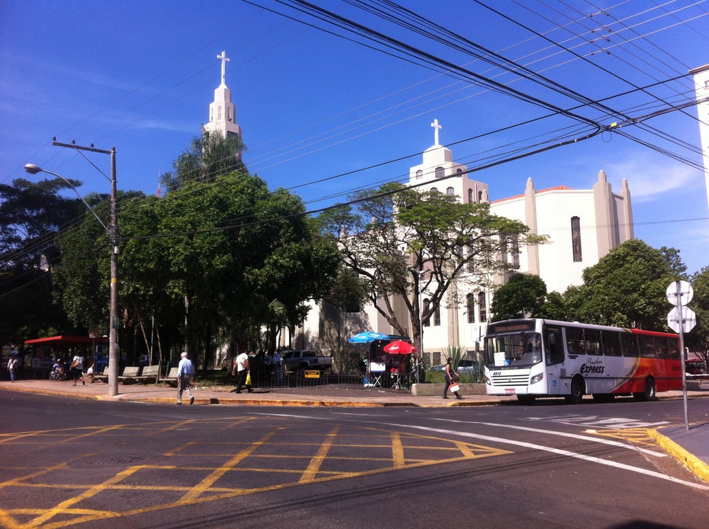 Cena urbana no interior paulista, com igreja e movimento de pedestres, ilustrando a região de Presidente Prudente/Alta Paulista