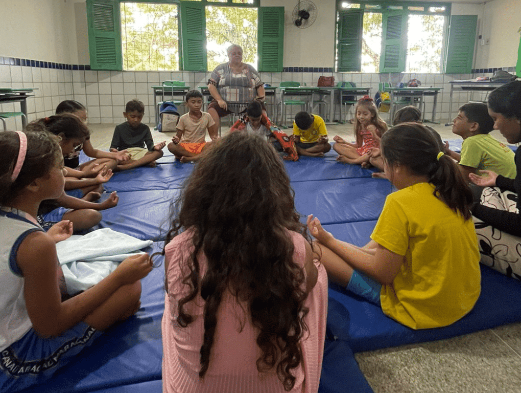 Sala de aula pública no interior do Nordeste, com crianças em atividade e professora ao fundo