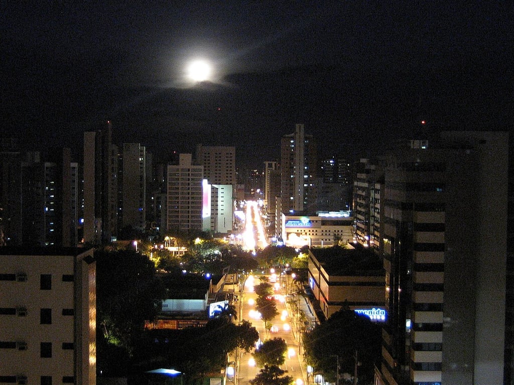 Vista noturna de Ribeirão Preto com edifícios iluminados e a lua ao fundo