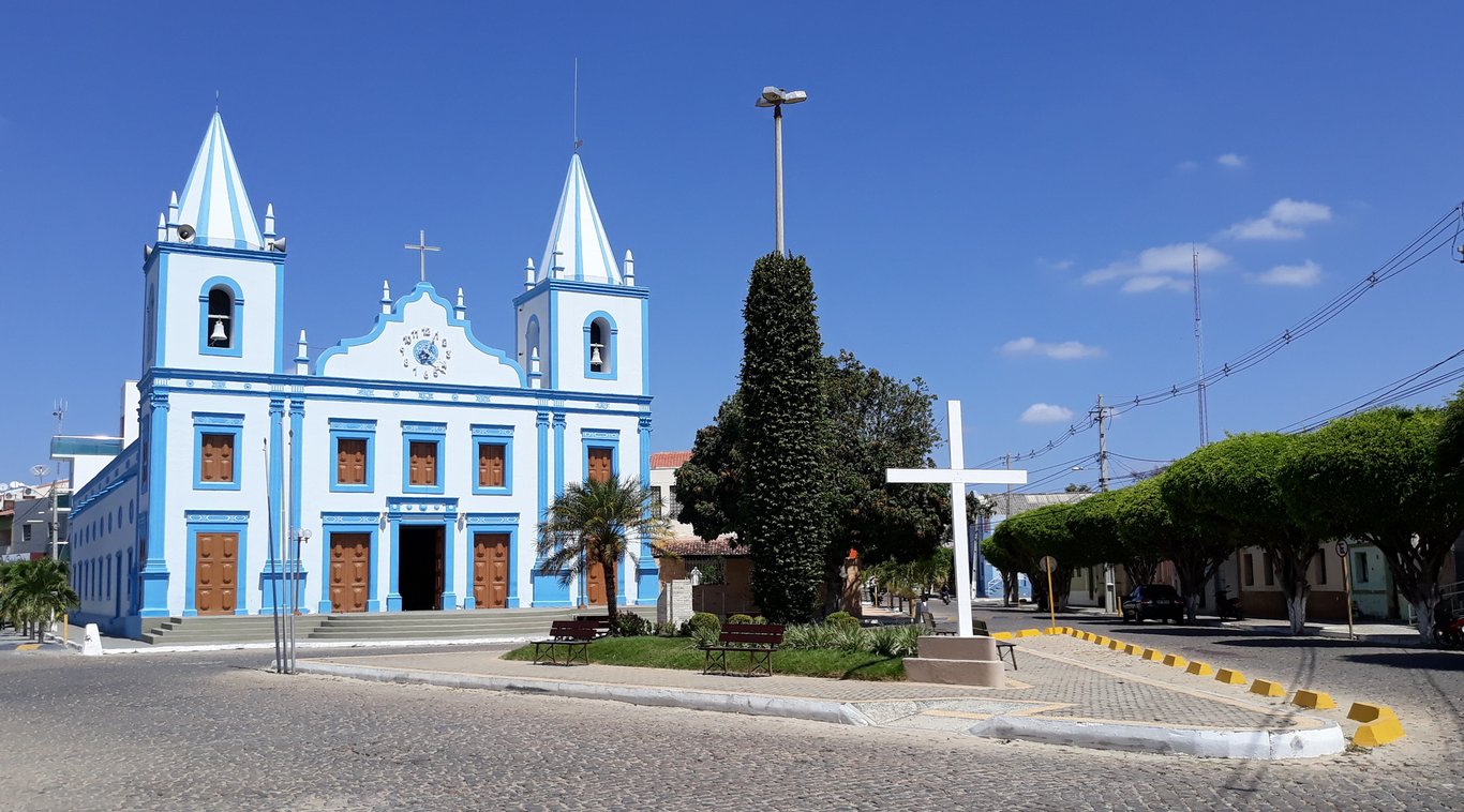 Vista urbana de Boa Saúde-RN, com igreja e praça central em dia ensolarado