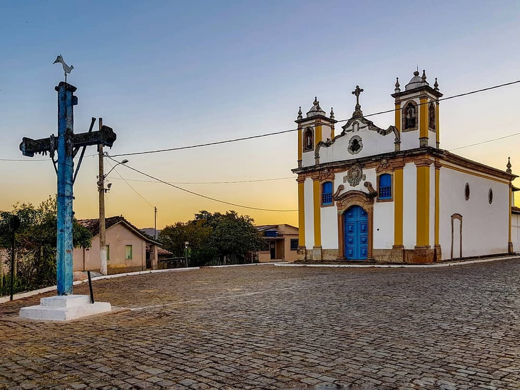 Centro histórico de Ibertioga MG, com igreja e cruzeiro em praça arborizada e céu azul ao fundo