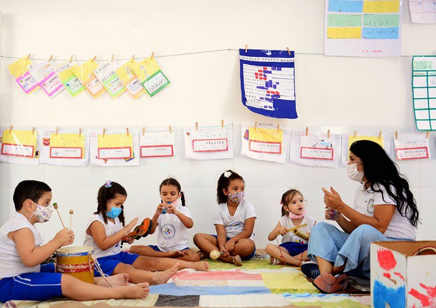 Sala de aula de Educação Infantil, com professora e crianças em atividades lúdicas