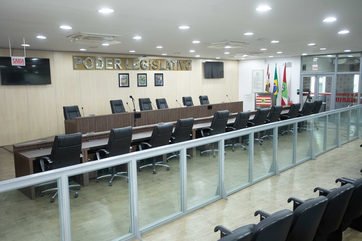 Plenário de câmara municipal, com cadeiras e púlpito ao fundo, em ambiente institucional iluminado.