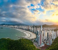 Vista aérea de Balneário Camboriú ao pôr do sol, com praia e skyline de prédios altos.