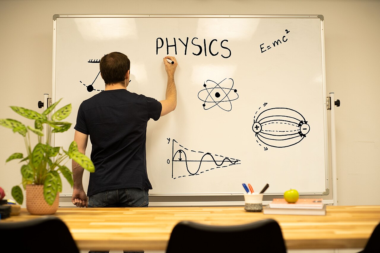 Sala de aula de Física com um professor escrevendo em um quadro branco.