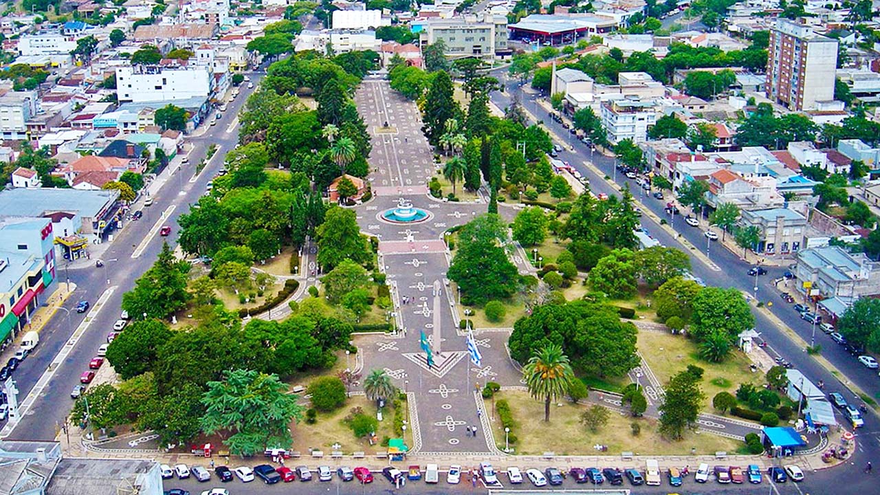 Vista panorâmica da Praça Internacional entre Santana do Livramento e Rivera, com área verde e prédios ao fundo sob céu azul.